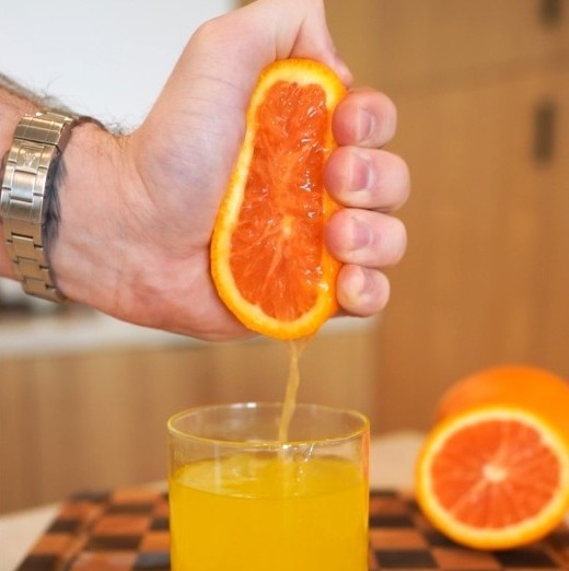 Hand squeezing fresh orange into glass of juice with Mood Mod orange cream saffron drink mix