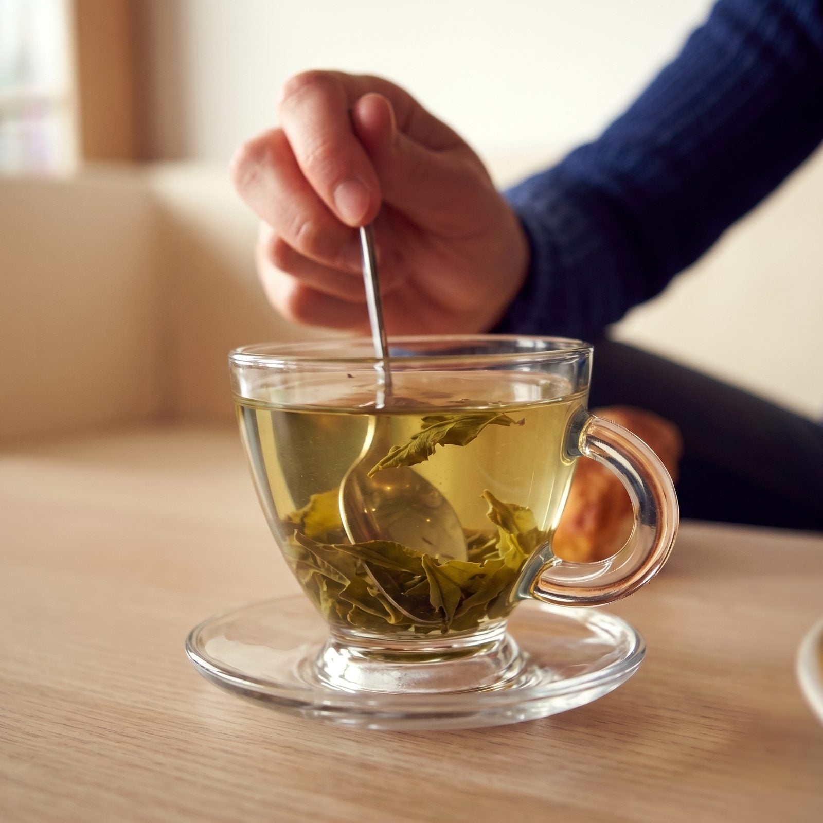 A person stirring a cup of green tea with loose leaves, the natural source of L-theanine for calm and better sleep