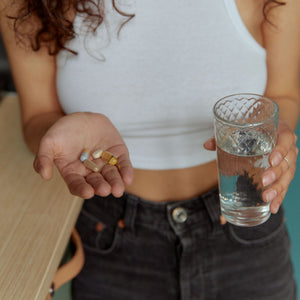 Woman holding a handful of supplement capsules and softgels in one hand and a glass of water in the other