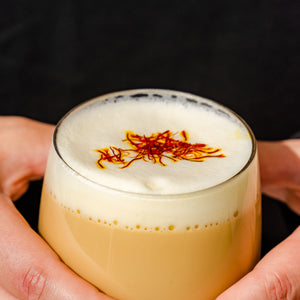 Hands holding a frothy saffron tea topped with saffron threads, showing saffron tea benefits for mood and sleep compared to saffron extract | Mood Mod