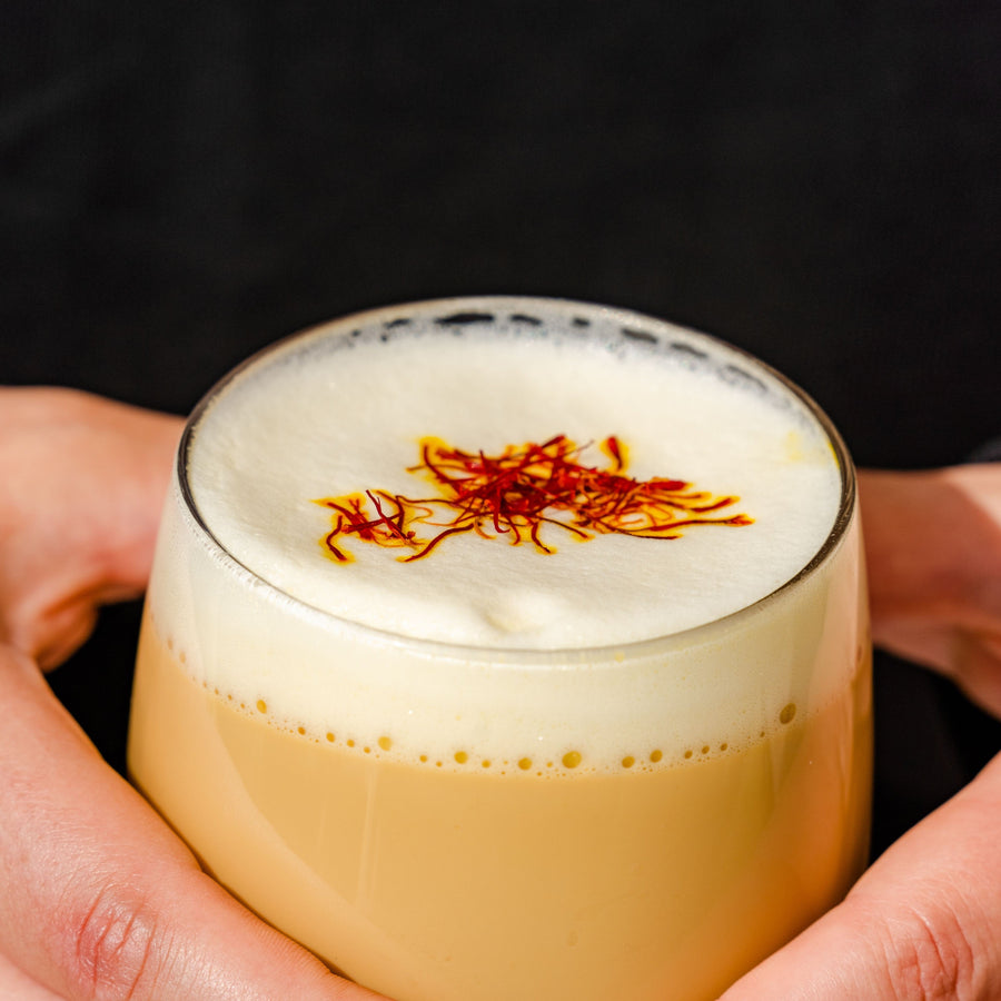 Hands holding a frothy saffron tea topped with saffron threads, showing saffron tea benefits for mood and sleep compared to saffron extract | Mood Mod