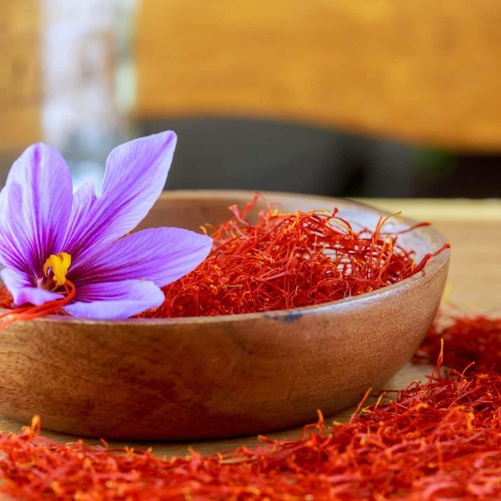 Saffron threads in a wooden bowl with a fresh purple Crocus sativus flower, the source of saffron extract used in Mood Mod.