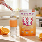 Mood Mod Orange Cream stick pack being poured into a water bottle next to the 20-count pouch and fresh oranges on a kitchen counter, showing 200mg L-Theanine, 30mg saffron, and 100mg magnesium glycinate.